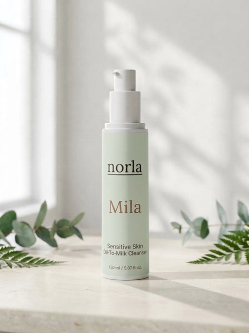 Mila Sensitive Skin Oil-To-Milk Cleanser 150 ml by Norla, white pump bottle with sage green label on a marble surface with eucalyptus and fern