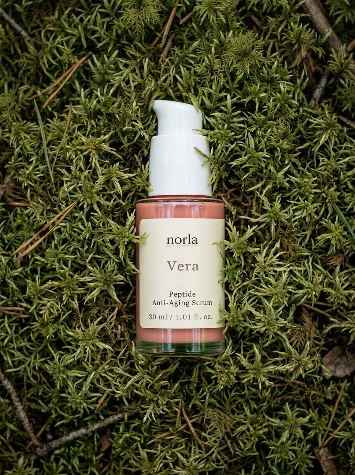 Vera Peptide Anti-Aging Serum 30 ml by Norla, rose-coloured glass pump bottle lying on green moss